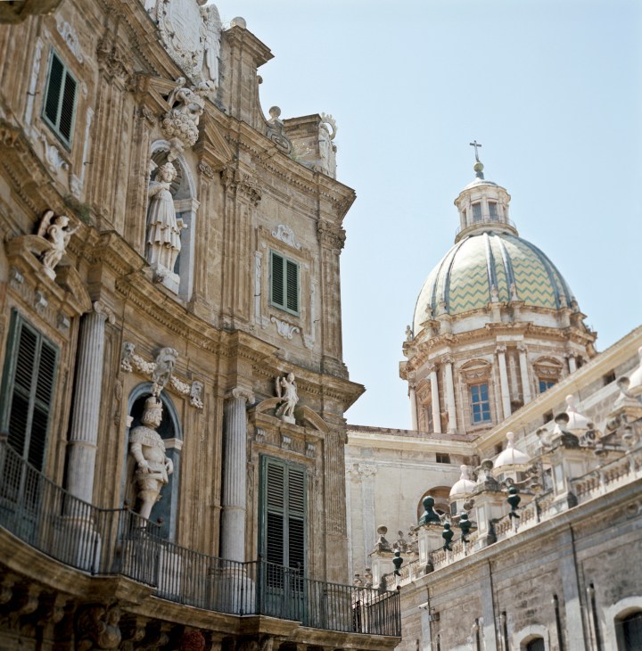 Ornate baroque buildings with sculptures and a domed church with a patterned dome at the Quattro Canti intersection in Palermo.