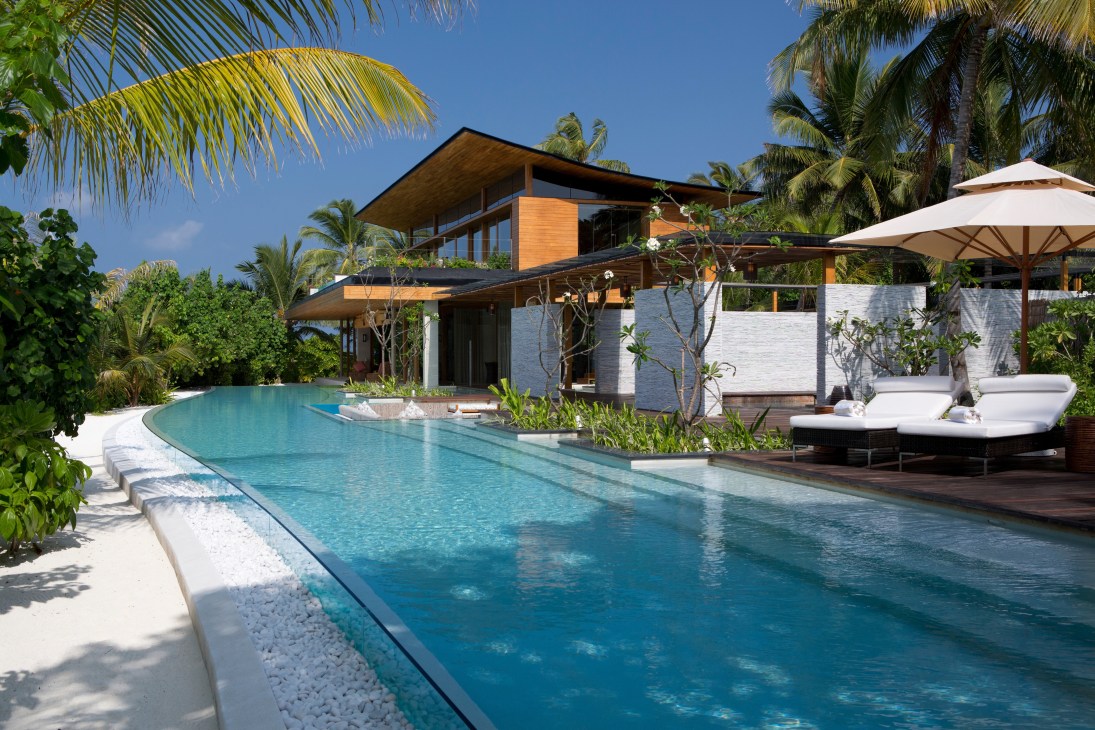 Modern teak house with pool surrounded by palm trees on Coco Privé island in the Maldives.