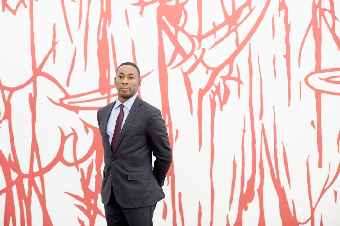 Franklin Sirmans stands in a dark suit against a red and white abstract artwork at the Pérez Art Museum.
