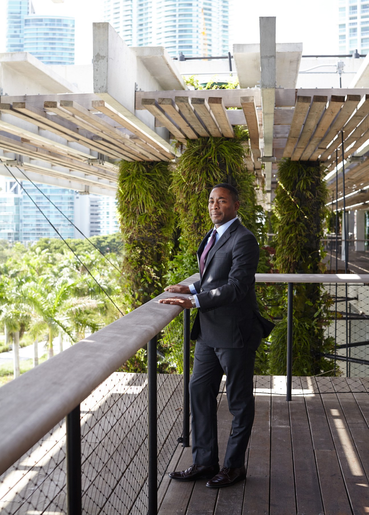 Franklin Sirmans stands at a railing on a rooftop terrace with hanging green plants and Miami's skyline in the background.