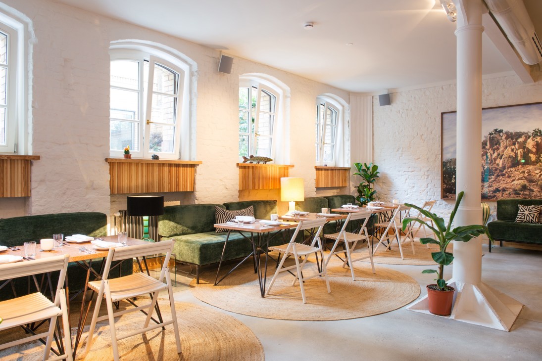 Panama restaurant dining room in Berlin with green banquettes, wooden chairs, arched windows, and potted plants.