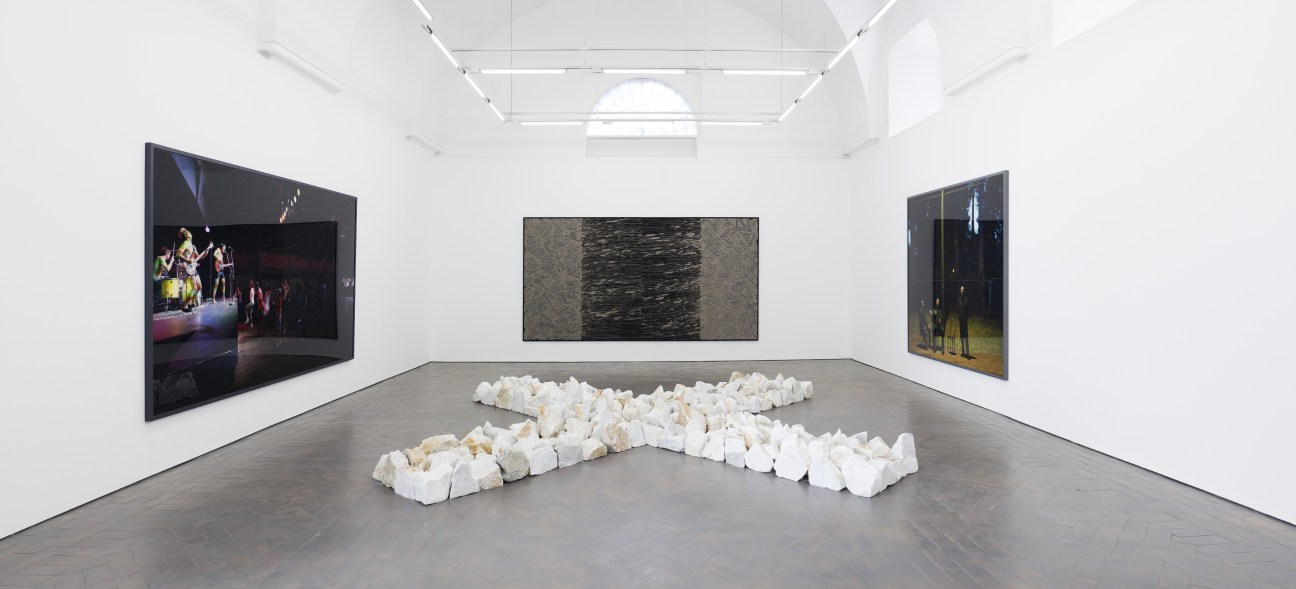 Gallery interior with Richard Long stone cross installation, mud canvas, and Jeff Wall photographs on white walls.