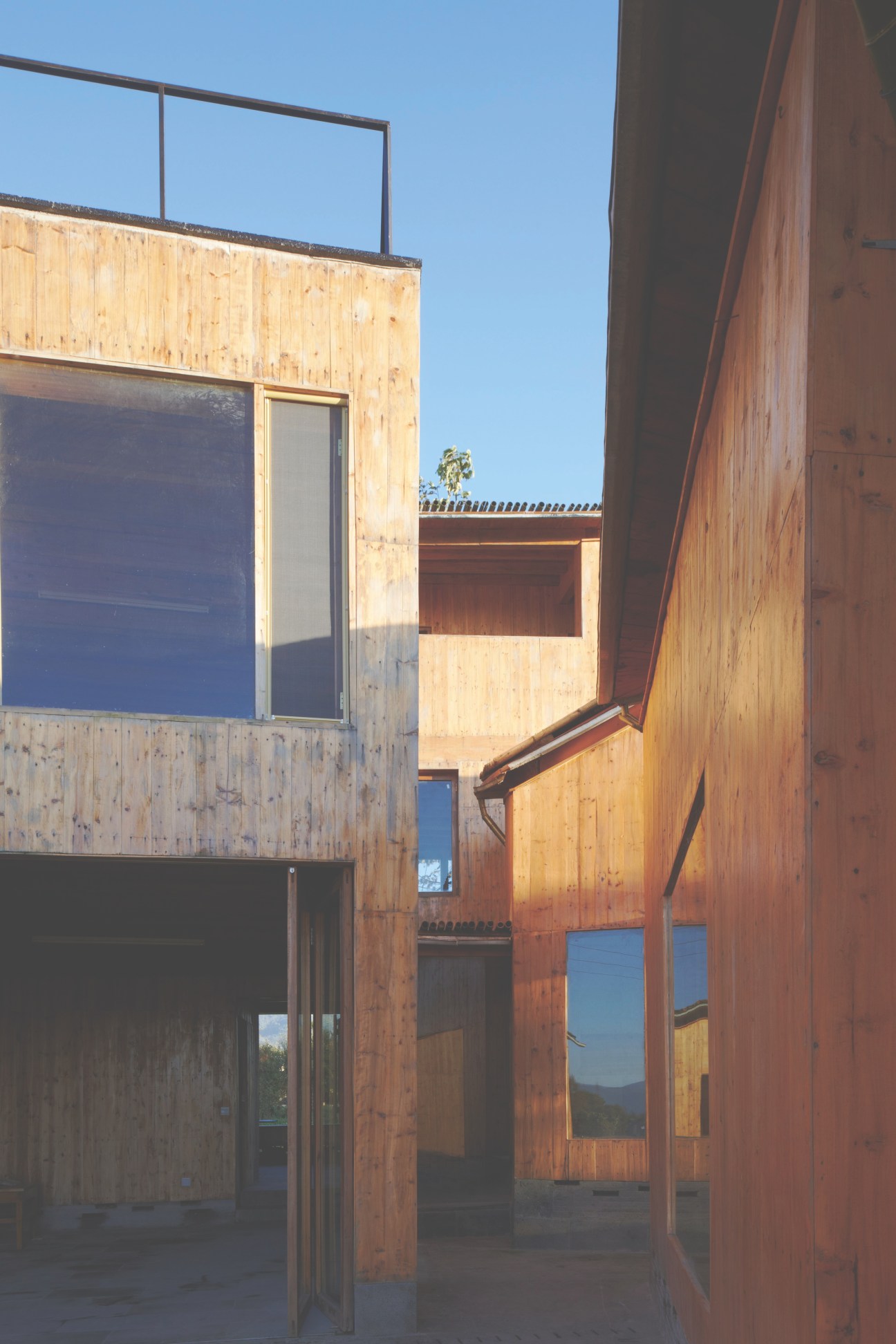 Modern timber and concrete buildings with wooden cladding and large windows under clear blue sky.