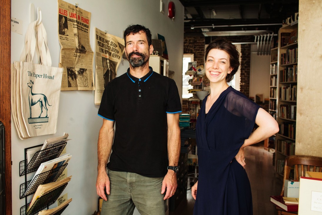 Rod Clarke and Kim Koch, co-owners of The Paper Hound bookshop, stand inside their Vancouver store surrounded by books and vintage newspapers.