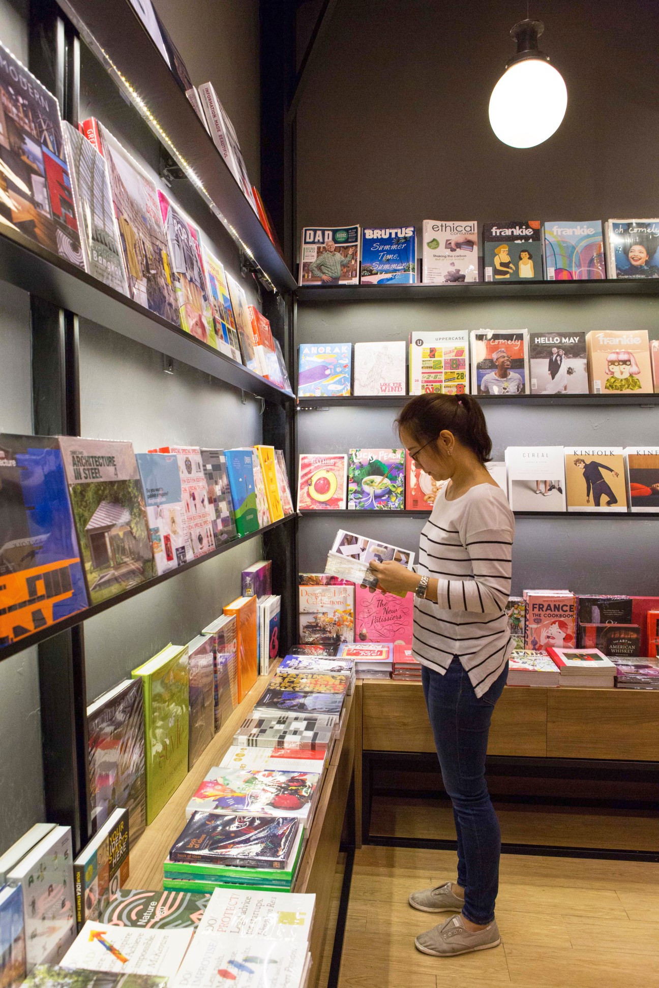 Woman browsing magazines in modern bookstore with shelves displaying international design and lifestyle publications