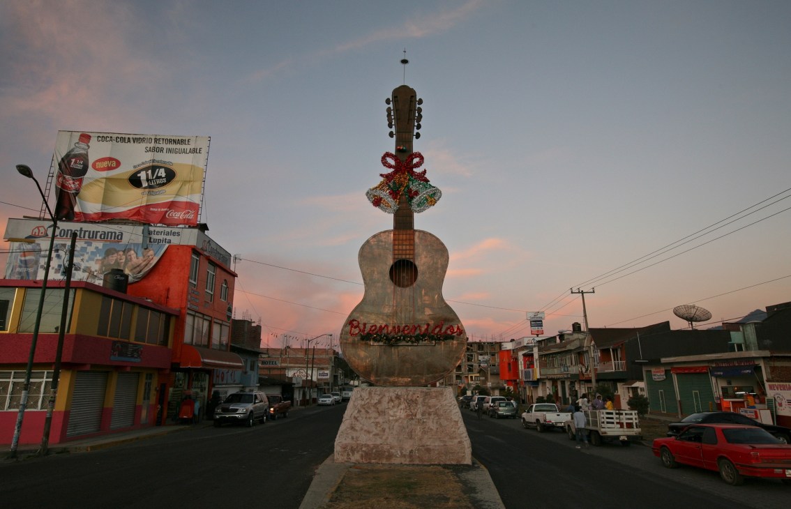 A giant copper guitar statue with holiday decorations stands at the entrance to Paracho, Mexico, welcoming visitors to the guitar-making town.