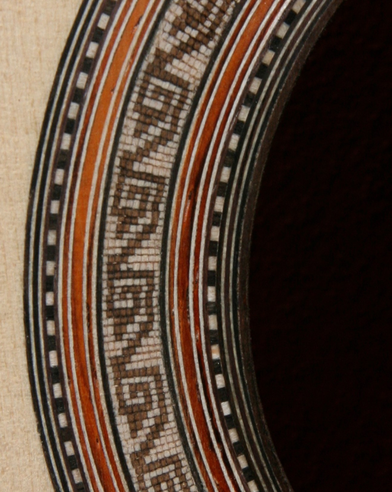Close-up of an intricate wooden rosette inlay surrounding a classical guitar's sound hole, featuring geometric patterns.