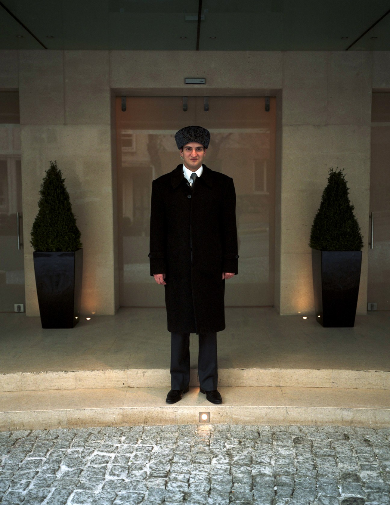 Park Hyatt Istanbul staff member in formal black coat and fur hat standing in modern lobby entrance.