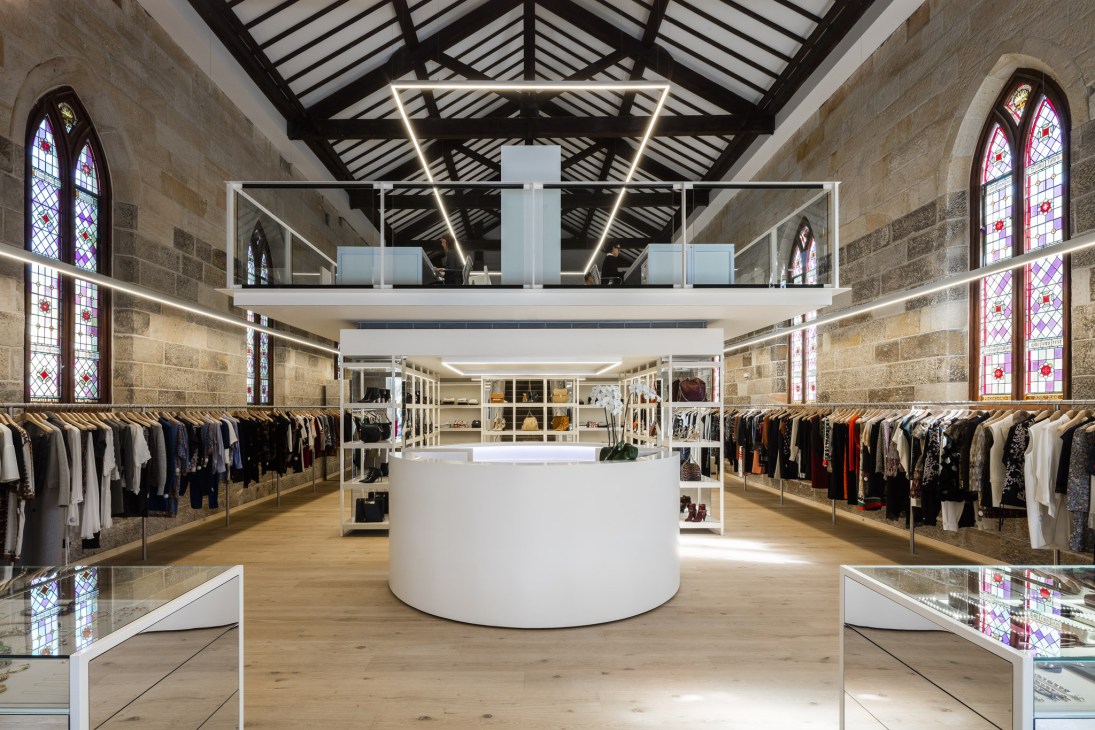 Interior of Parlour X boutique in a converted church featuring stained-glass windows, sandstone walls, modern lighting, and clothing displays.
