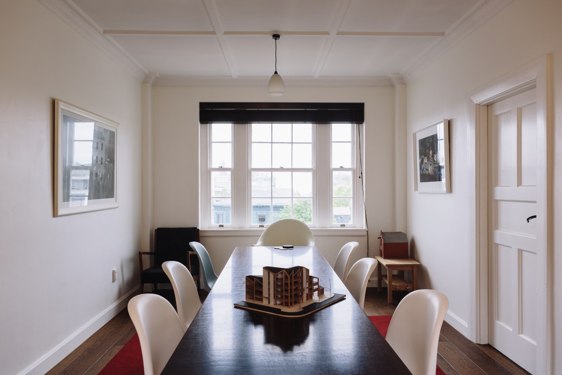 Modern dining room with black table, white chairs, and architectural model displayed on surface.