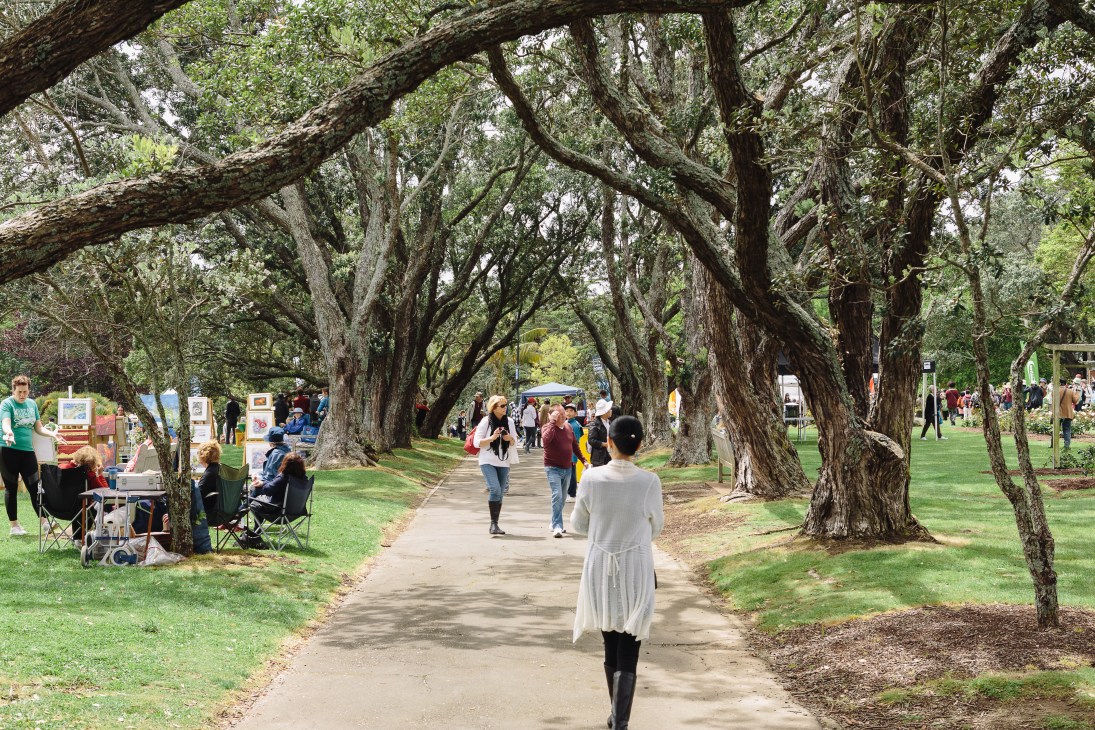 People walking through shaded pathways lined with large pohutukawa trees at Parnell Rose Gardens in Auckland.