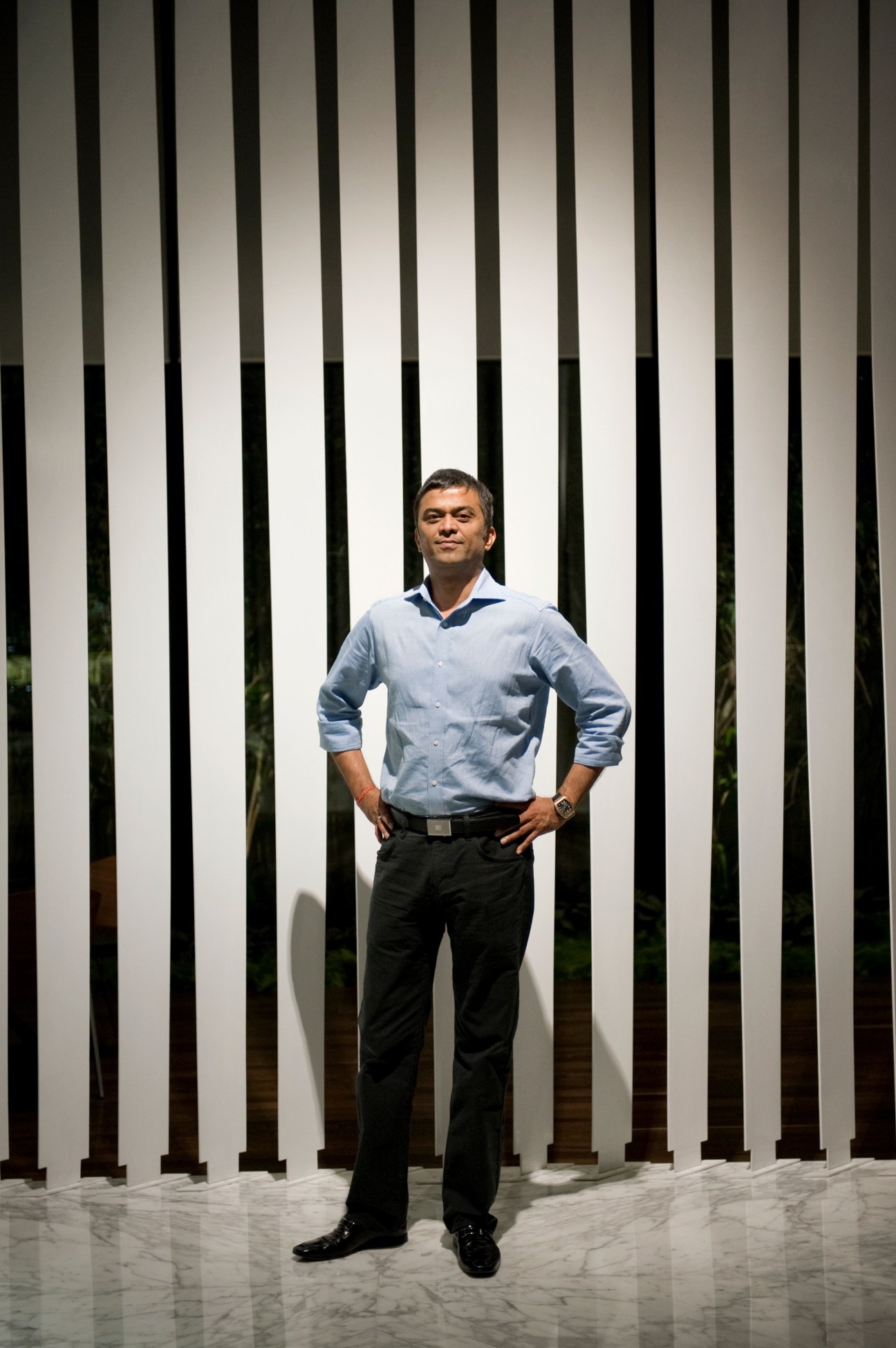 Rahul Saraf, developer of the Atmosphere building, stands with hands on hips against a striped wall backdrop.