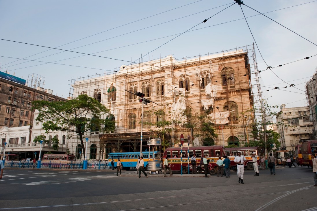 Colonial-era building under renovation with scaffolding, surrounded by historic architecture and street traffic in central Kolkata.