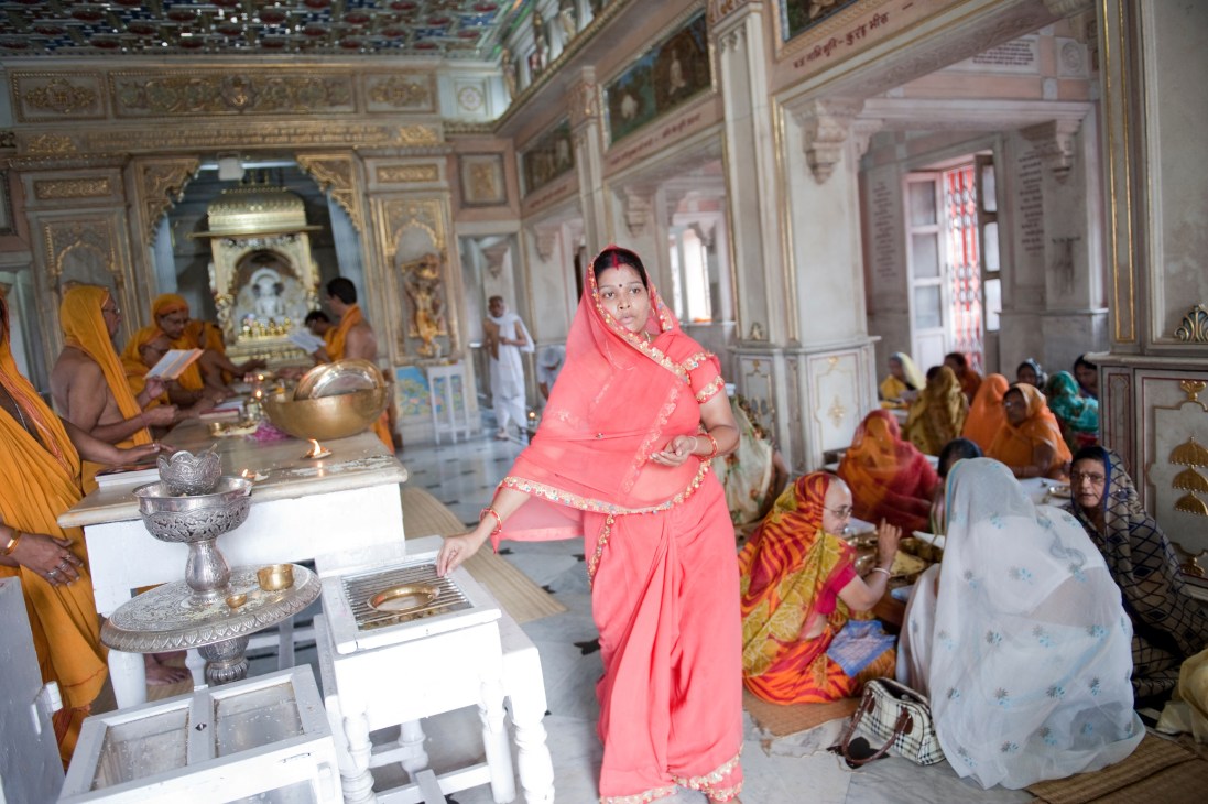 Interior of a Jain temple in Kolkata with ornate gold-decorated walls, devotees in traditional dress, and religious artifacts.