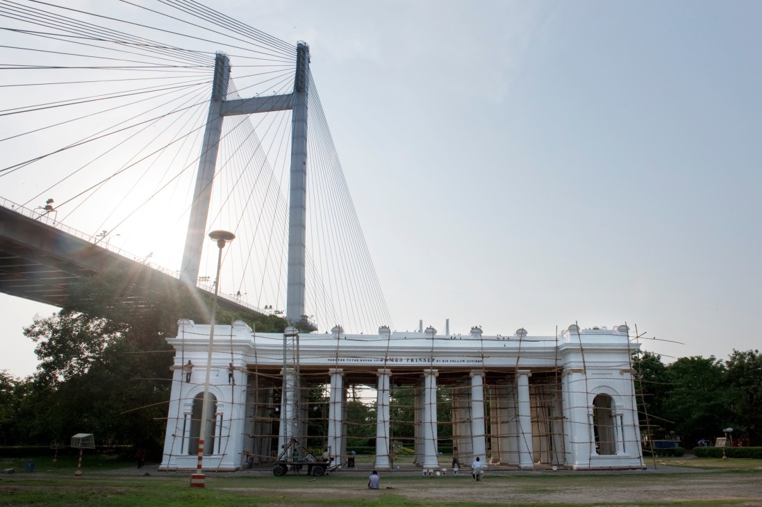 Princep Ghat's white colonial structure with columns under the Vidyasagar Setu Bridge spanning the Hooghly River in Kolkata.