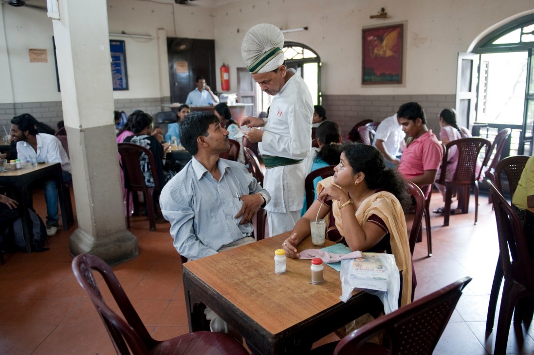 A server in traditional white attire and turban serves customers at a table inside the Indian Coffee House in Kolkata.