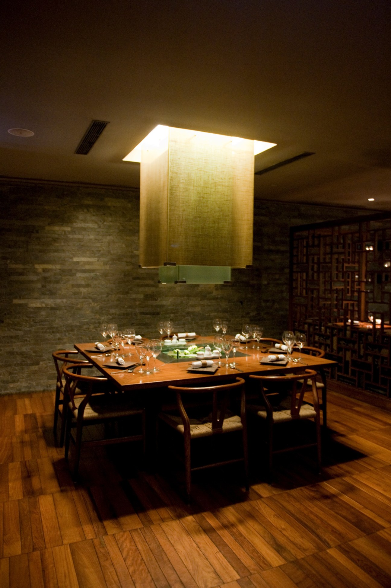 Modern dining room with round wooden table, mid-century chairs, and illuminated geometric pendant light above.