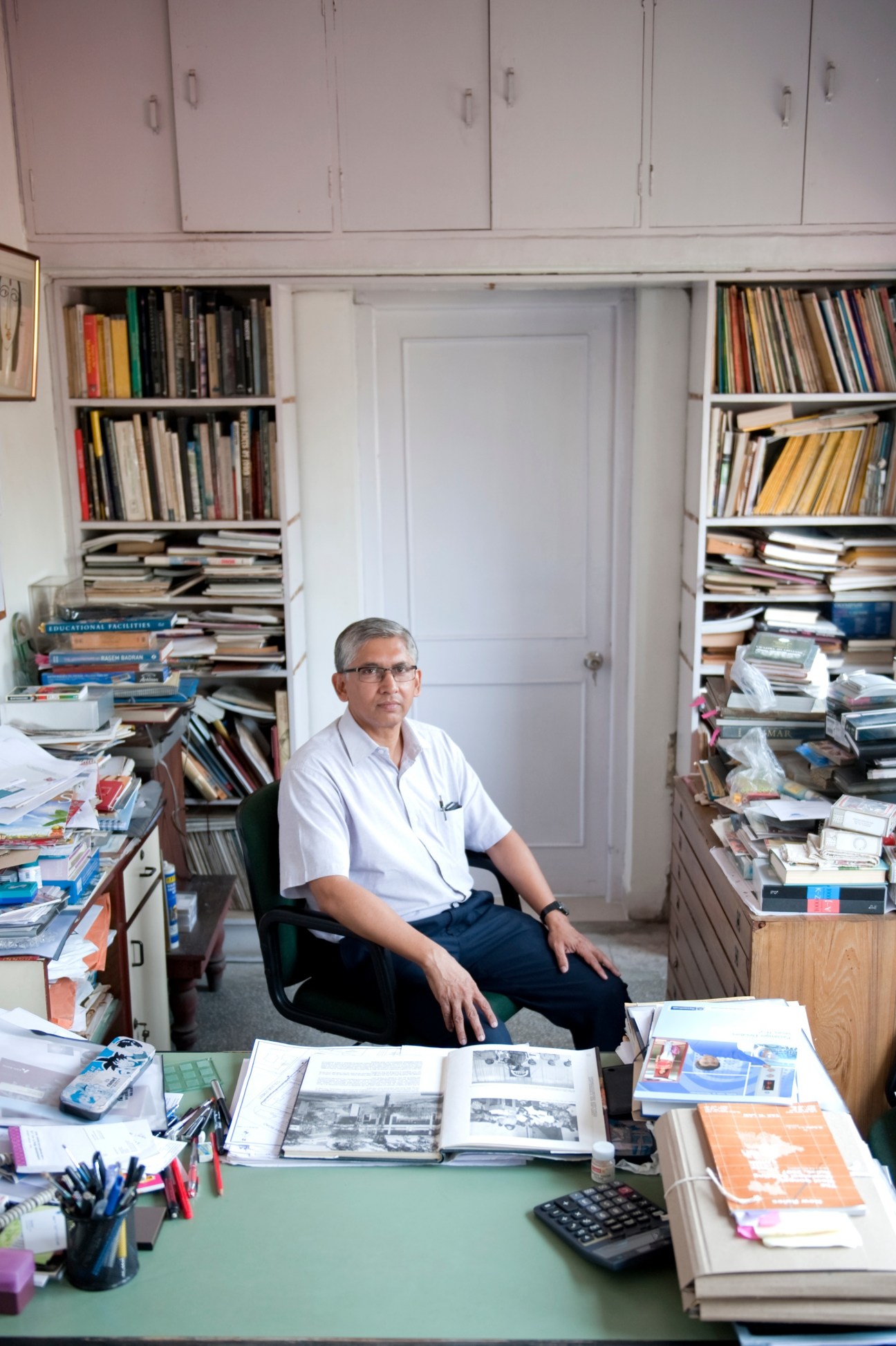 Architect Partha Ranjan Das sitting in his office surrounded by bookshelves and architectural documents.