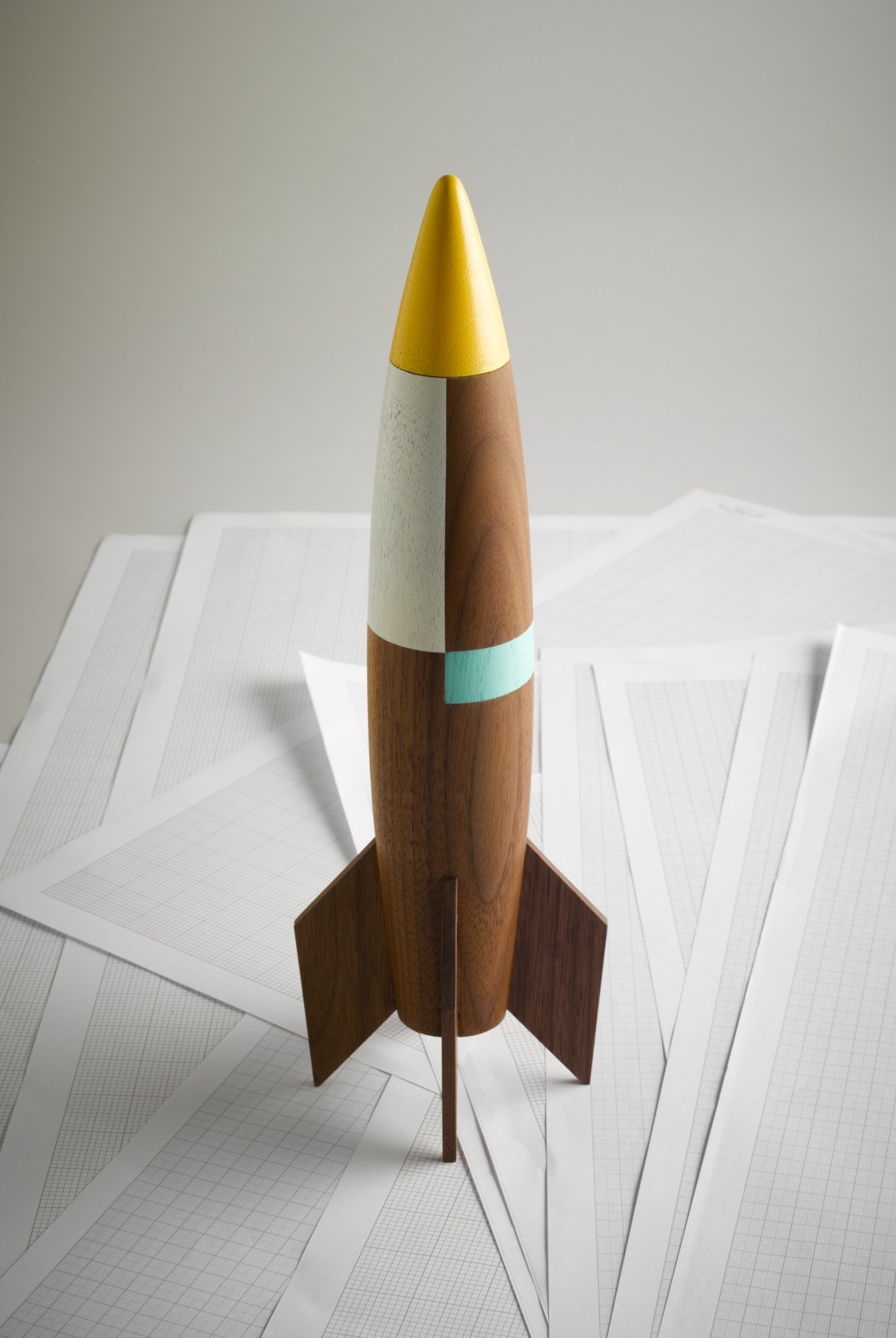 Handmade wooden rocket toy by Pat Kim with yellow nose cone, natural and brown wood body, turquoise band, and wooden fins.