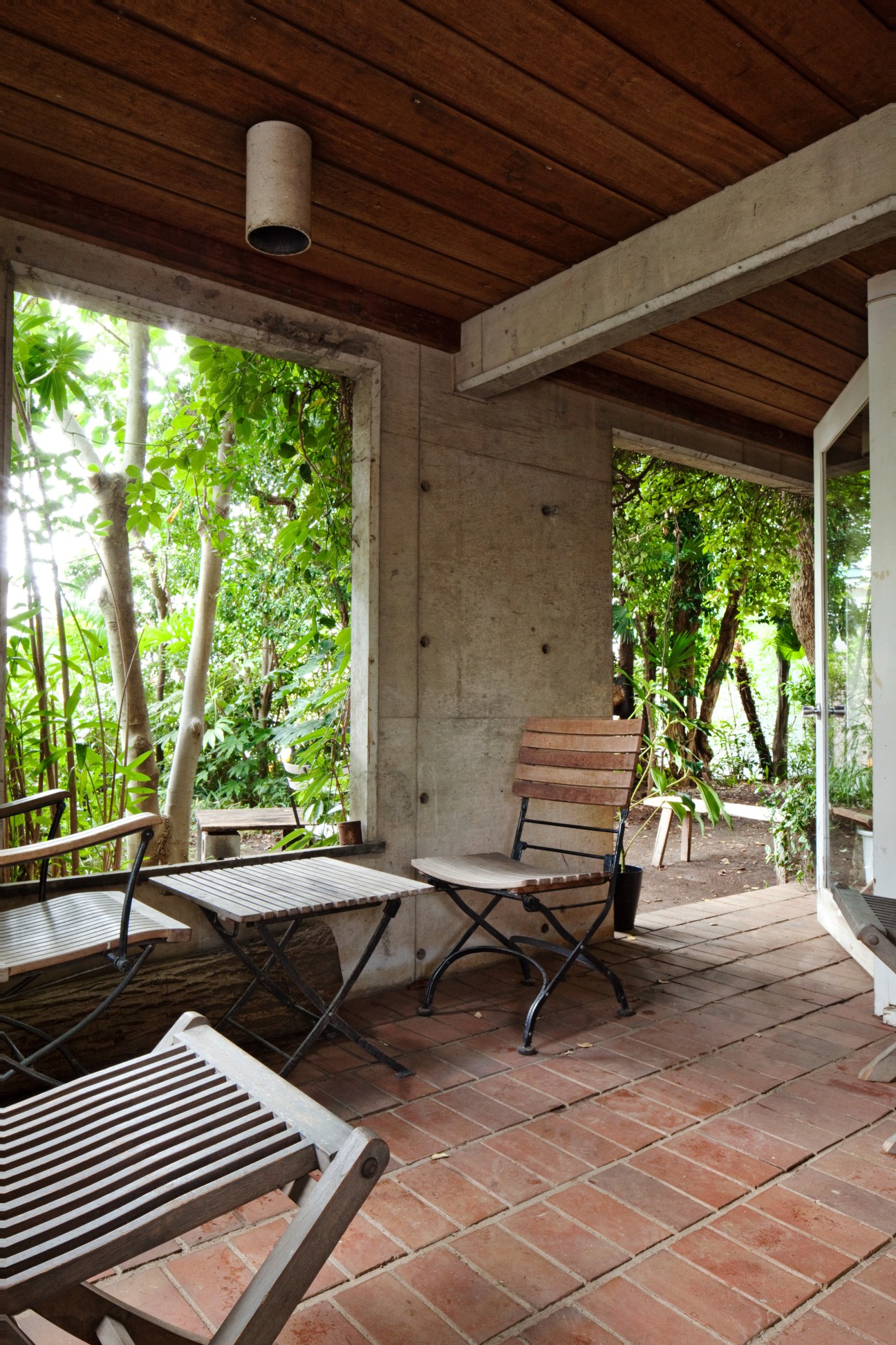 Covered terrace with wooden ceiling, folding chairs, and terra cotta tile floor overlooking lush garden