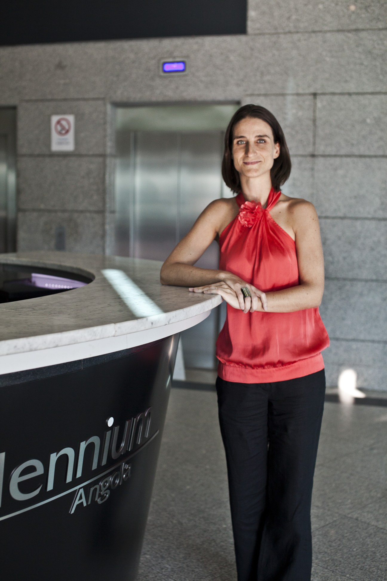 Patricia Teixeira, 32, stands at a modern reception desk wearing a red halter top.