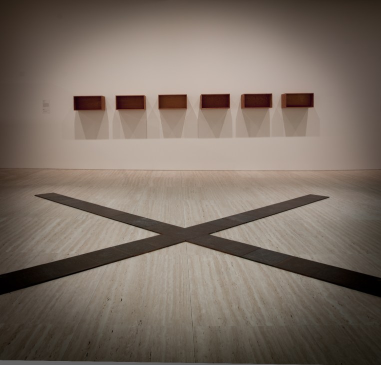 Gallery interior with Carl Andre's dark wooden floor sculpture and Donald Judd's wall-mounted boxes