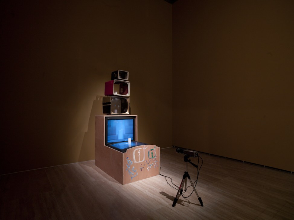 Nam June Paik's 'TV Buddha' artwork featuring stacked vintage televisions with a Buddha statue on a pedestal in a gallery space.