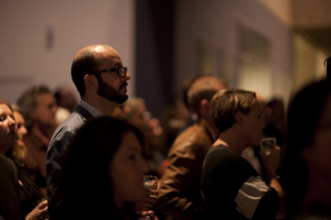 Guests at an art gallery opening party viewing exhibitions in a light-filled space.