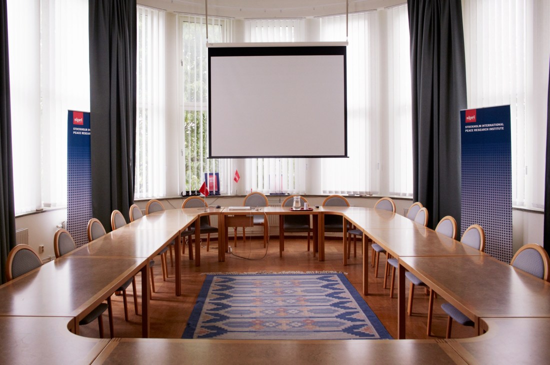 SIPRI's main conference room with long wooden tables, chairs, projection screen, and SIPRI banners.