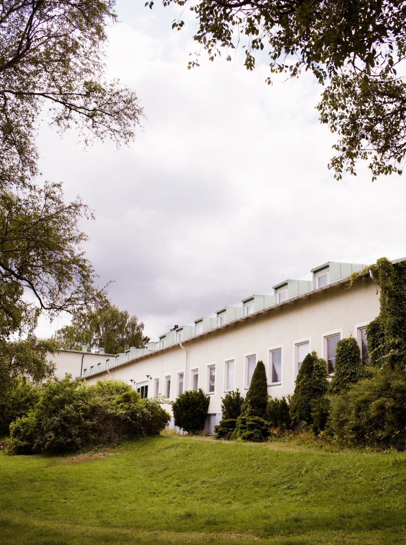 SIPRI's white building headquarters in Solna, Sweden, surrounded by green grounds and leafy trees.