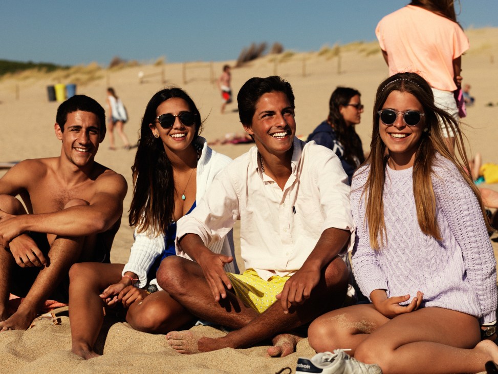 Group of smiling locals sitting on sand at Guincho Beach on a sunny day.