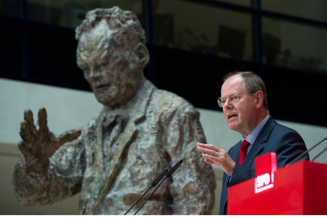 Peer Steinbrück speaking at a podium with a statue behind him.