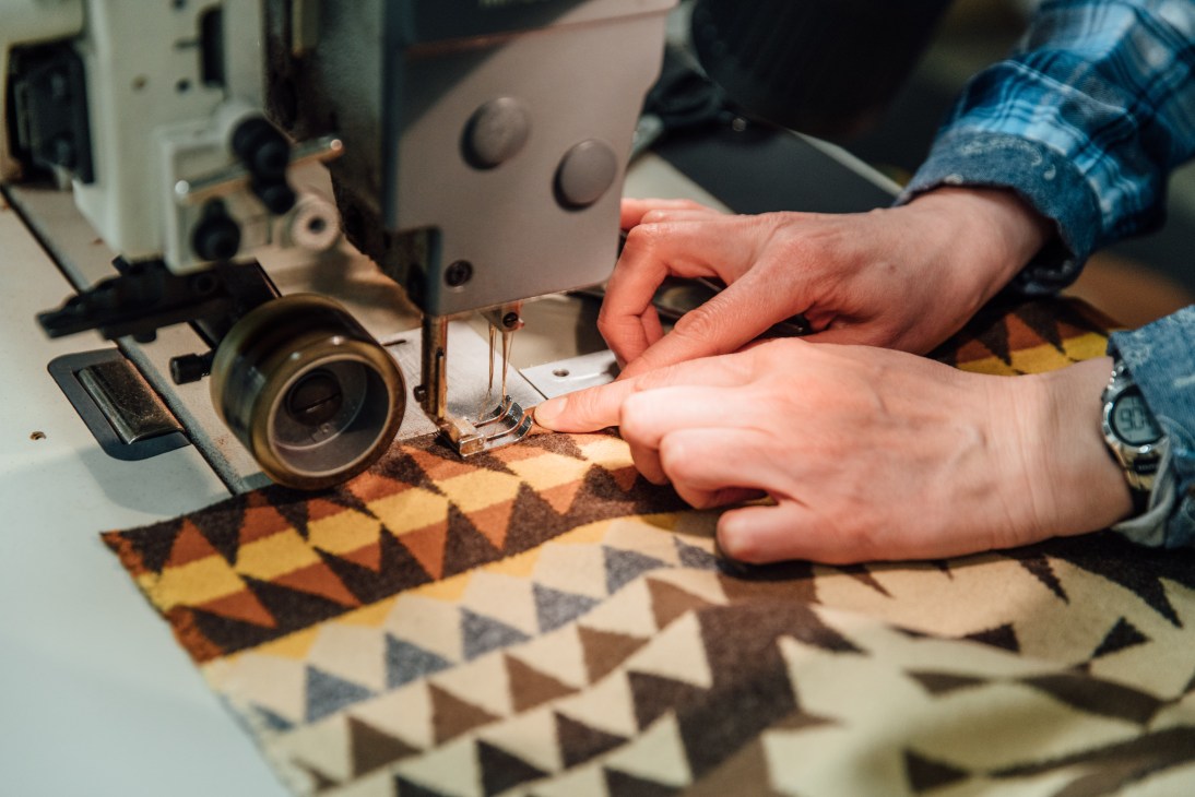 Worker sewing patterned fabric on an industrial sewing machine.