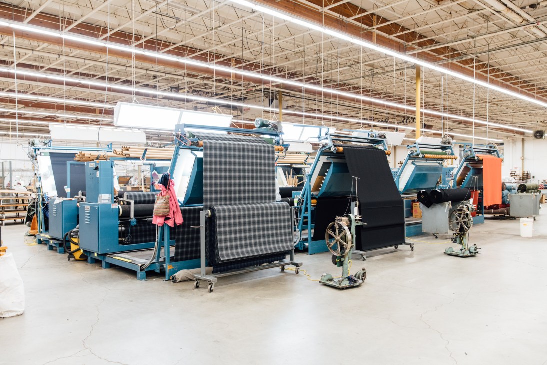 Textile factory production floor with blue industrial machinery processing patterned fabric rolls.