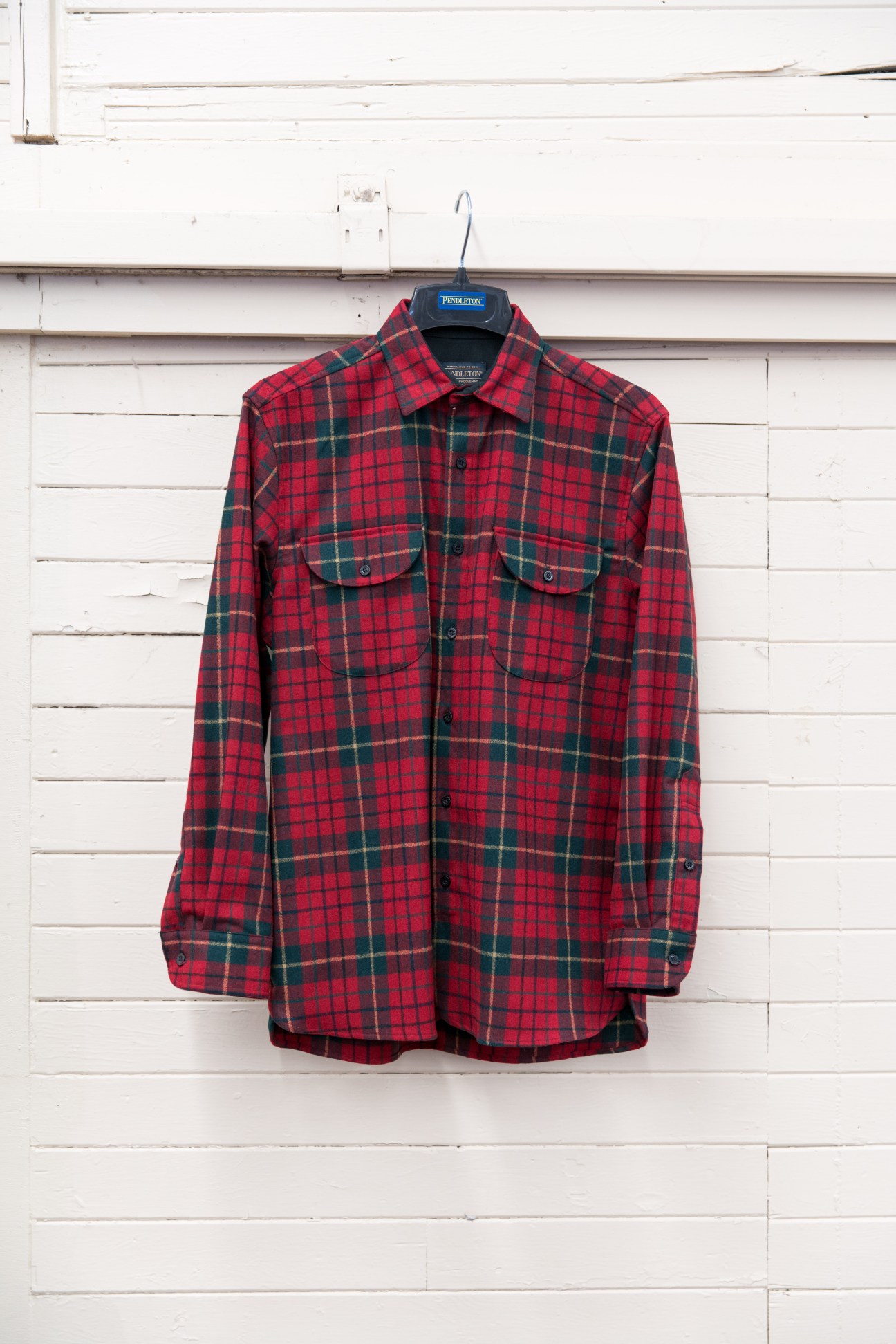 Red and green plaid wool Pendleton Fireside shirt displayed on hanger against white wall.