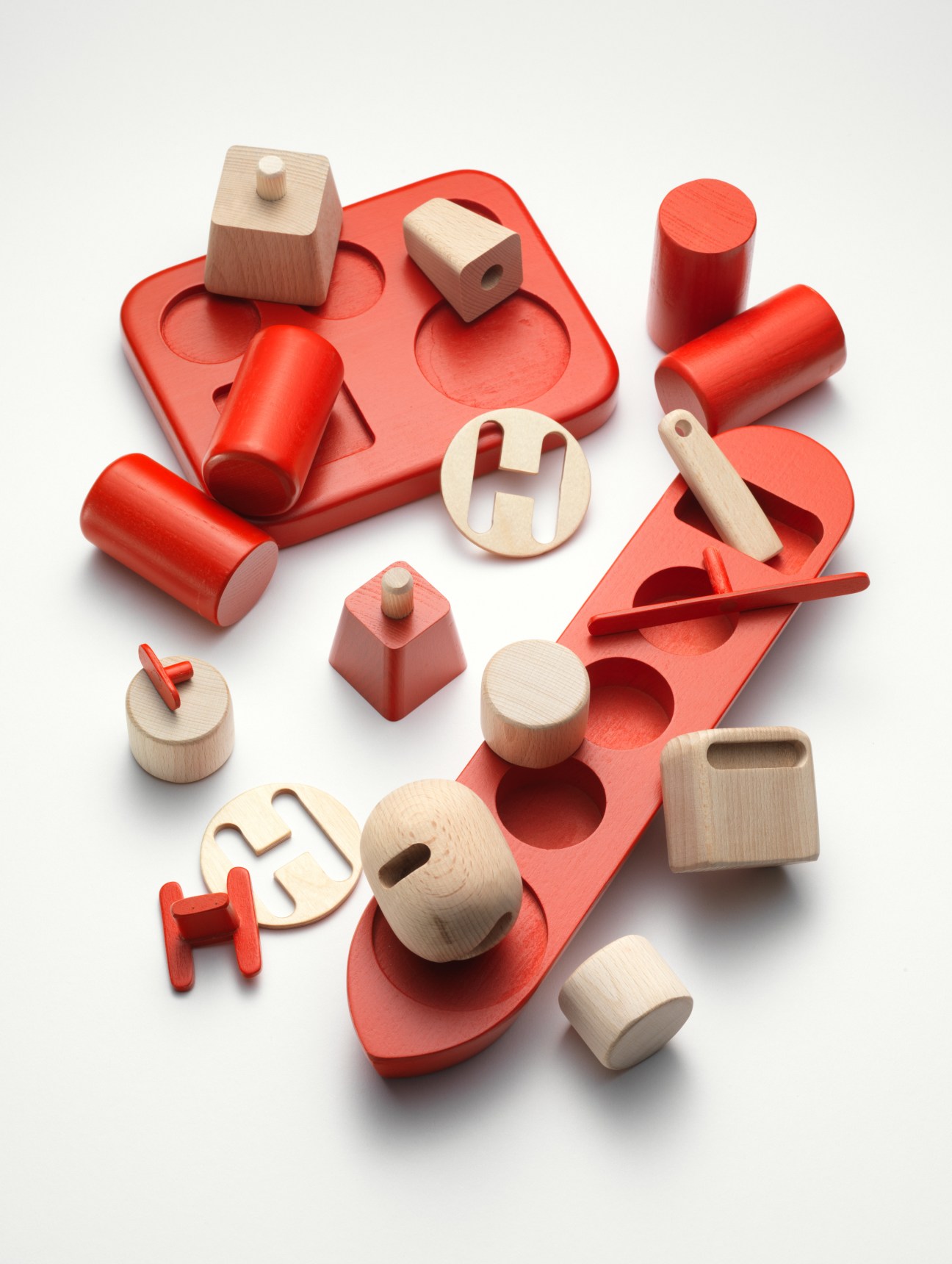 Wooden toy shapes and red blocks arranged on white background, including cylinders, cubes and circular pieces.