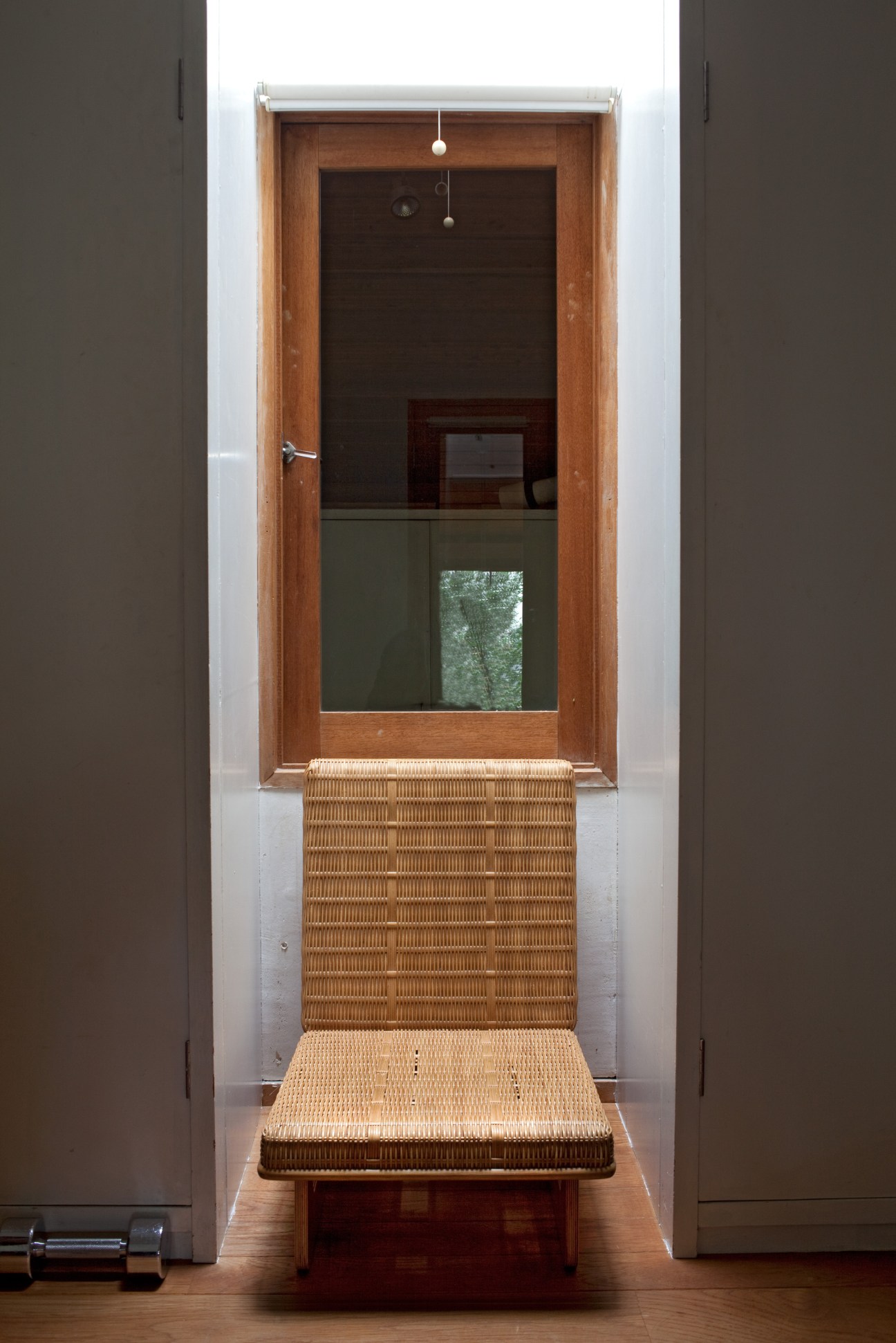 Woven rattan chair by Charlotte Perriand and Junzo Sakakura positioned between gray walls and doorway