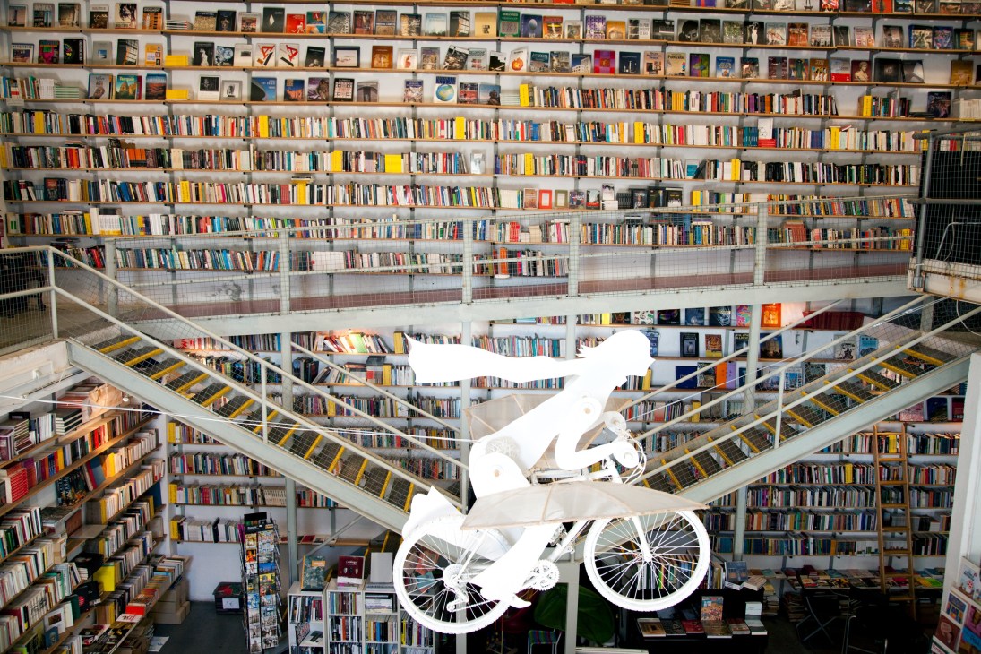 Interior of Ler Devagar bookshop in Lisbon with floor-to-ceiling shelves and a white bicycle sculpture suspended in the center.