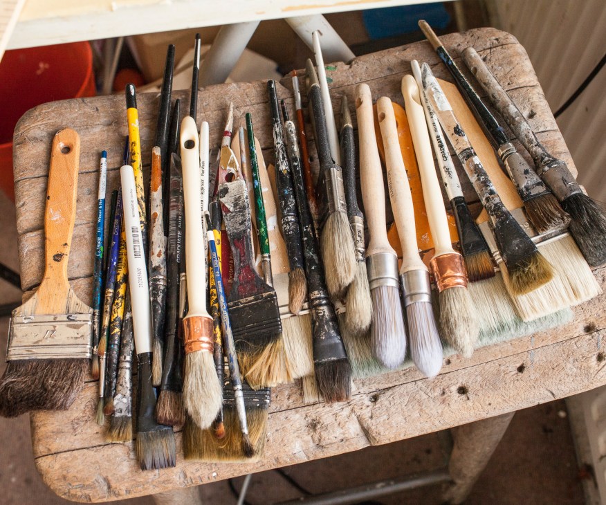 Collection of artist paintbrushes and tools arranged on weathered wooden palette.