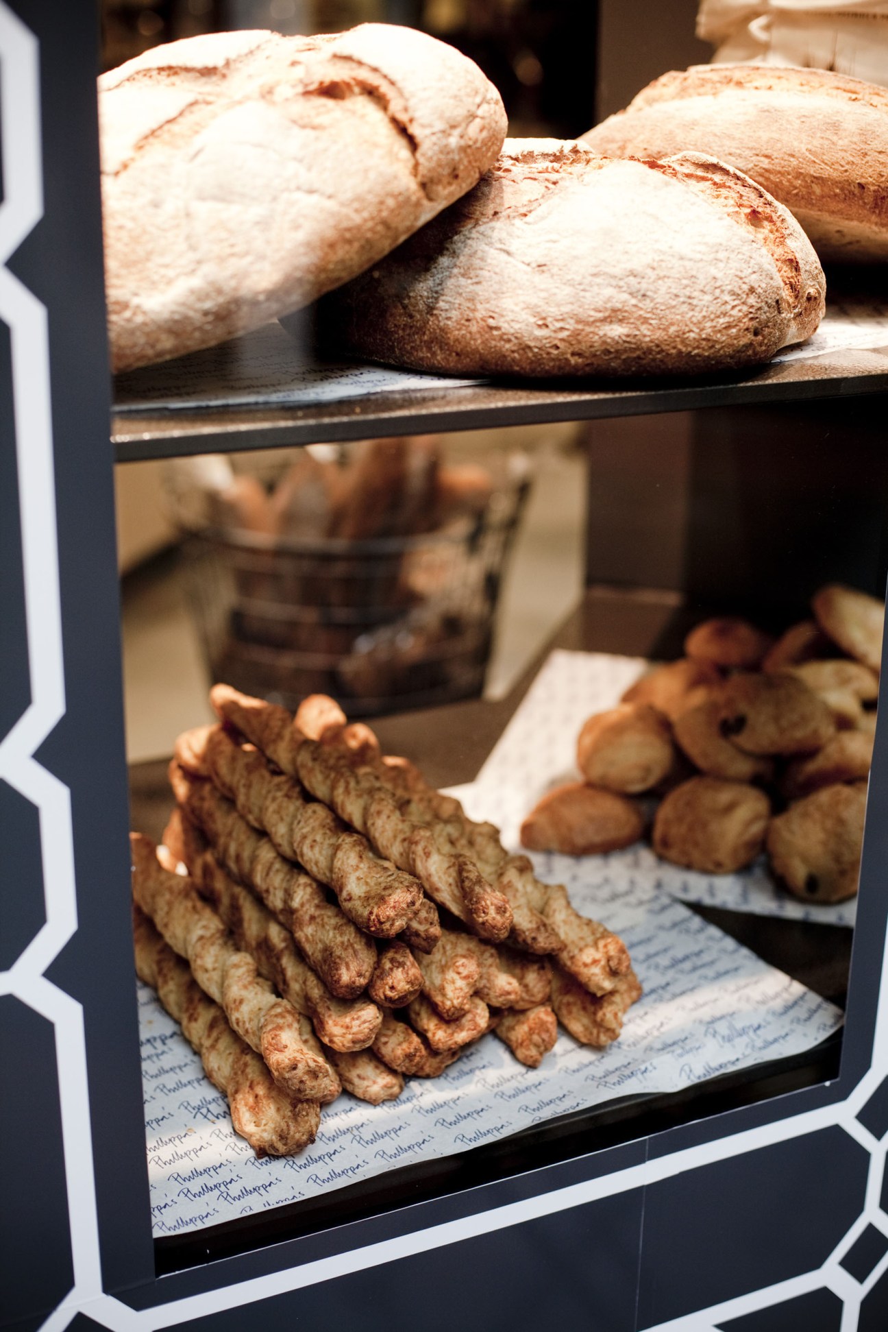 Bakery display case with crusty bread loaves and breadsticks on shelves.