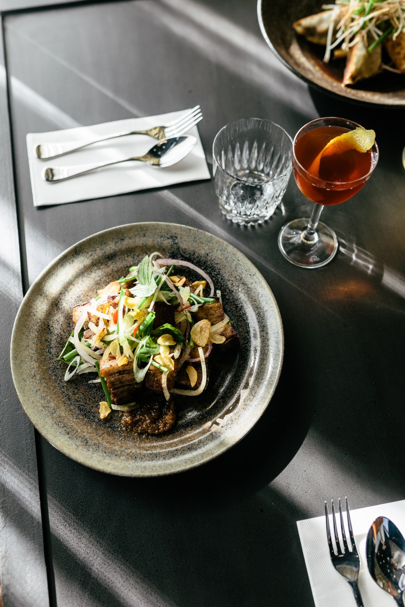 A plated dish with meat and vegetables at Sweetwater Rooftop Bar in Fremantle, served with cocktail and glassware.