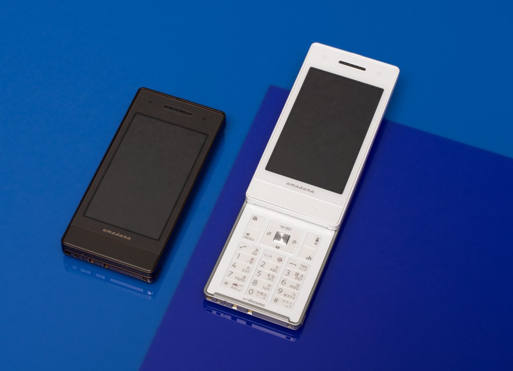 Two Amadana mobile phones on a blue background, one black and one white with open flip design.