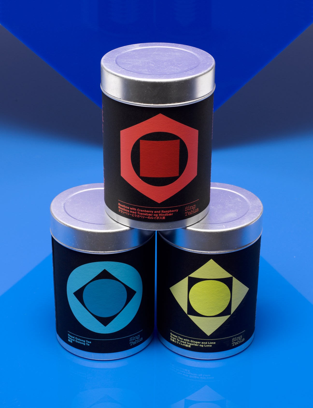 Three black cylindrical tea canisters with colored geometric logos on a blue background.