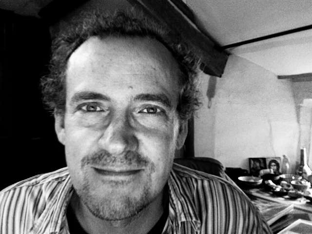 Black and white portrait photograph of Michael Axworthy, a man wearing glasses and a striped shirt.