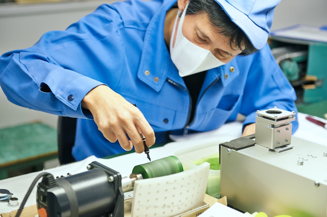 A Pilot factory worker in blue uniform and cap tests a fountain pen nib on equipment.
