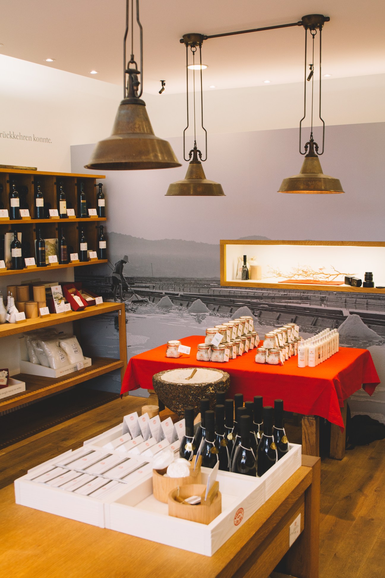 Interior of Piranske Soline salt shop featuring wooden shelves, brass pendant lights, and displayed products on tables with red cloth.