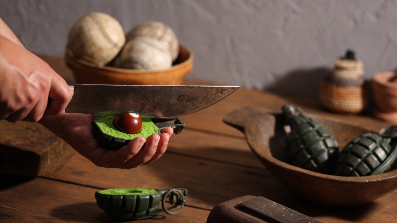 Stop-motion animation scene from Fresh Guacamole showing a knife cutting a grenade-shaped avocado on a wooden surface.