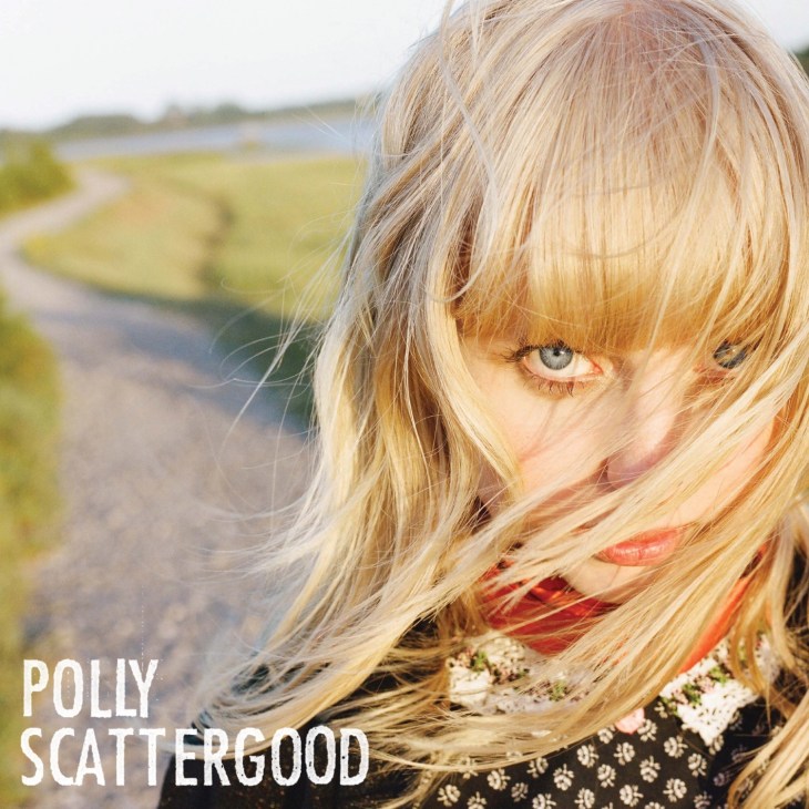 Polly Scattergood with blonde hair and fringe looking at camera in countryside setting