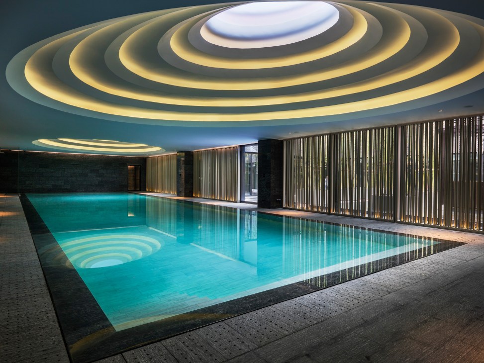 Indoor swimming pool with turquoise water and concentric circular lighting design on ceiling.