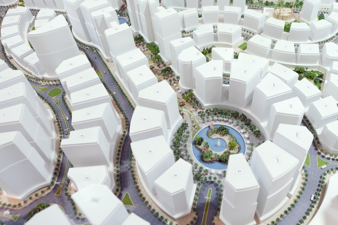 Aerial view of Al Hilal City model plan showing white curved towers with green spaces and central pond.